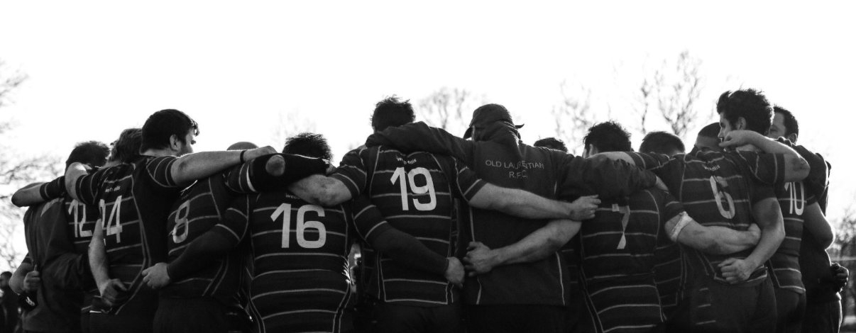A rugby team huddled in a circle, arms linked around each other's shoulders
