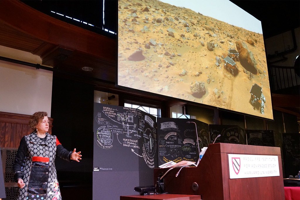 Astronomer Alyssa Goodman speaks beneath a giant projection of the Martian surface with rovers, flanked by hand-drawn graphic-recording panels.
