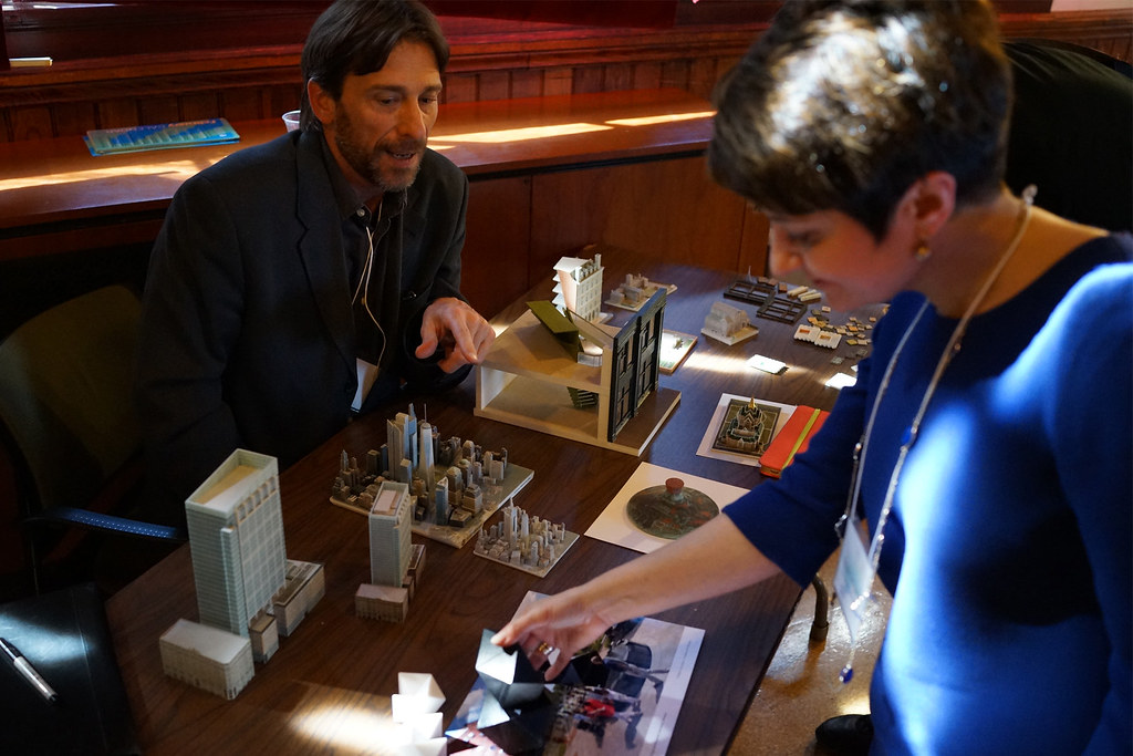 Two attendees lean over a table of 3D-printed architectural and city models, examining a miniature skyline.