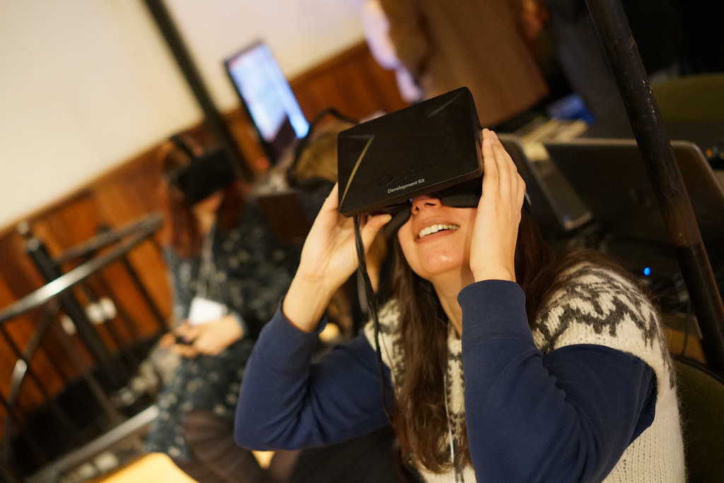 A smiling attendee holds a virtual-reality headset to her face while others wait their turn behind her.